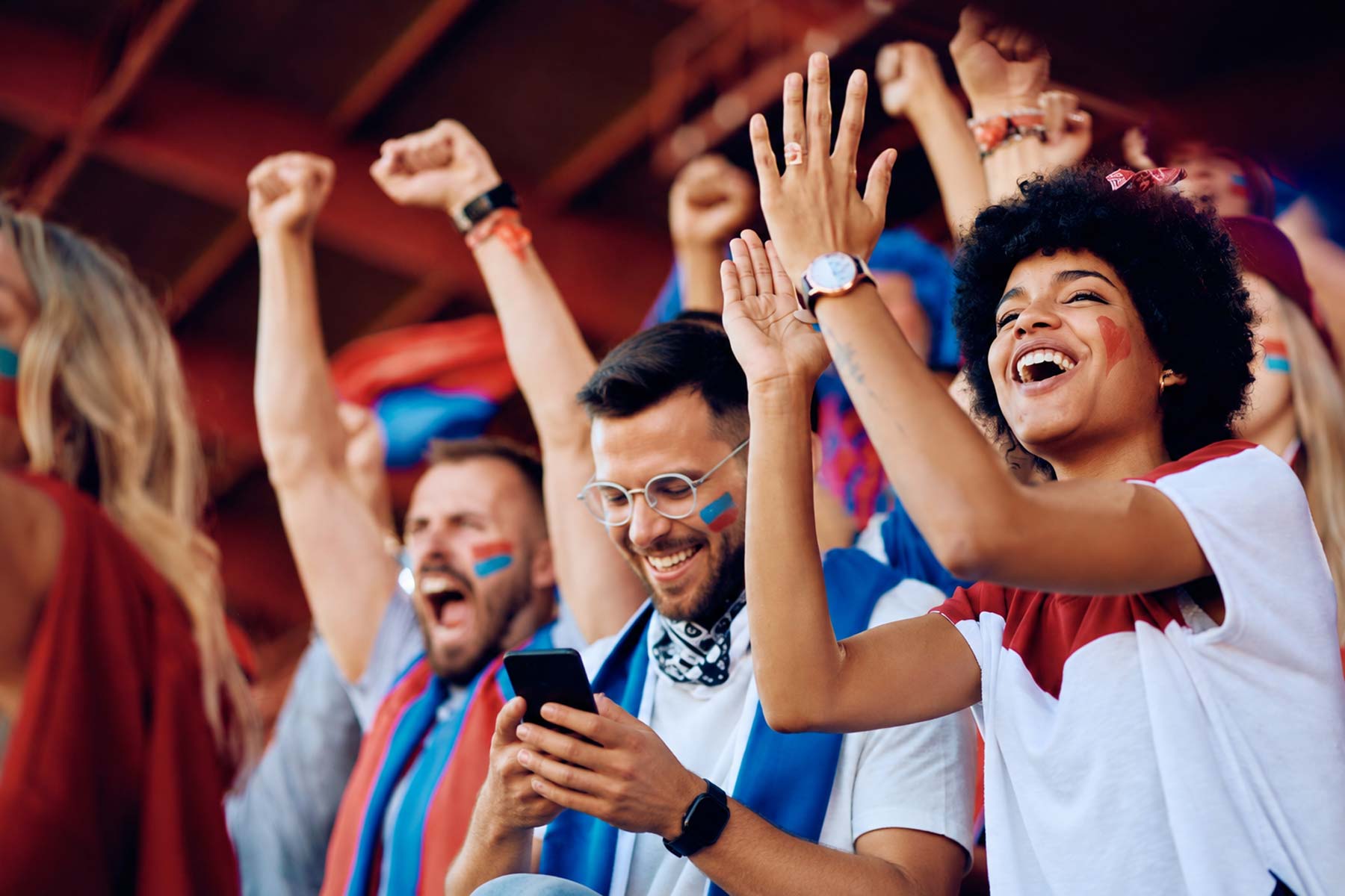 Fans in a stadium cheering with one fan looking at an SMS marketing message from the team
